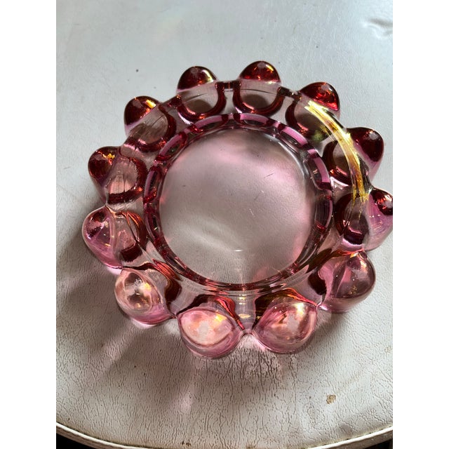striking mid-century style ashtray crafted from thick glass with a subtle pink tint. The round form is accented with a...