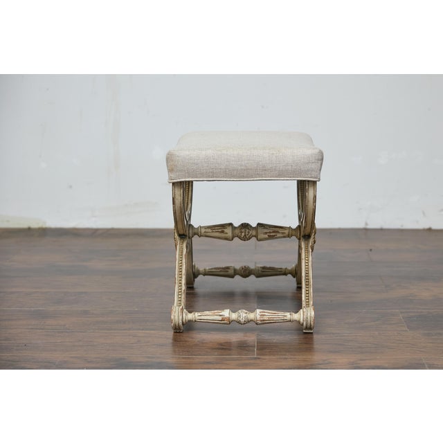 A French Empire style painted wood curule stool from circa 1900 with gilded accents, curved X-shaped legs, carved...