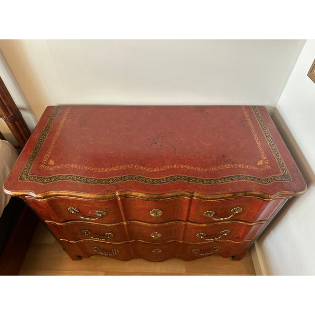 An exceptional Theodore Alexander three-drawer chest featuring a richly patinated crimson-red leather-wrapped exterior,...