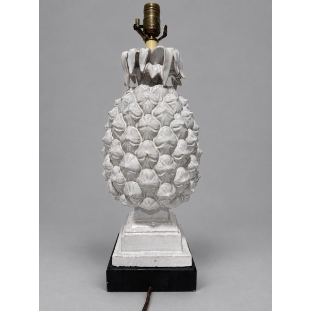 A decorative white glazed ceramic table lamp modeled in pineapple form, with a deeply textured body composed of raised...