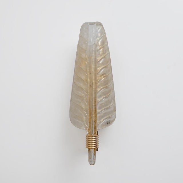 An elegant pair of italian wall sconces with sculptural murano glass lampshades shaped like stylized leaves. Each finely...