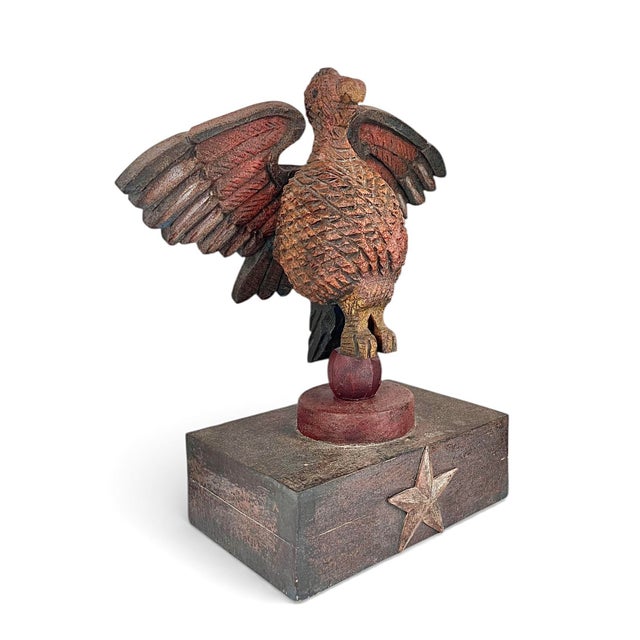 A nicely carved and painted folk art sculpture of an eagle with outstretched wings perched on a ball, all sitting atop a...