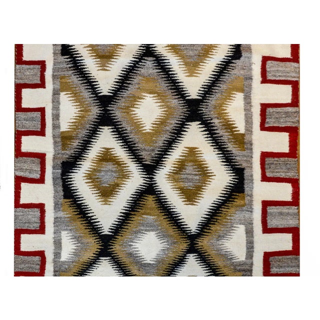 A bold mid-20th century Navajo rug with an all-over diamond pattern woven in black, white, and brown wool surrounded by a...
