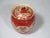A vintage porcelain hand painted covered jar with scalloped edge. It has a brick red background, decorated with intricate...