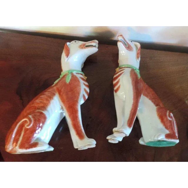 A pair of Samson figures of hounds in the Chinese taste decorated in iron red with green collar and gilt bells. A true...