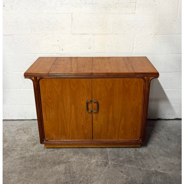 Vintage mid-century modern dry bar featuring warm honey-toned wood veneer, flowing grain, and layered molding with gently...