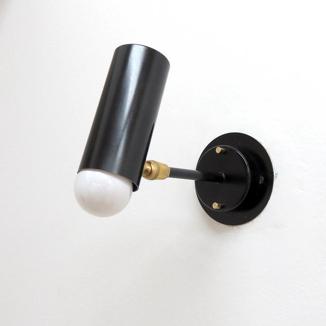 Elegant articulate wall lights, in black enameled metal with brass accents, swivel joint at the cylinder, complementary...
