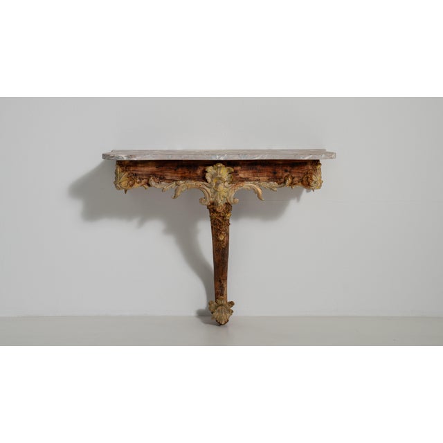 An early 19th century French Rococo-style console table with a patinated finish and a marble top, showcasing the graceful...