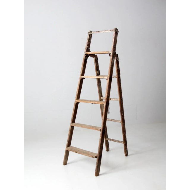 This is a vintage wooden folding ladder. The a-frame ladder features five rung steps with a chain link center. Folds for...