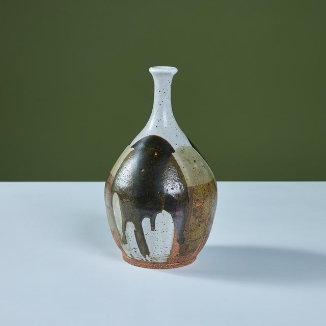 Hand thrown stoneware bud vase features a small spout opening and varying colors of drip gaze throughout the form in...