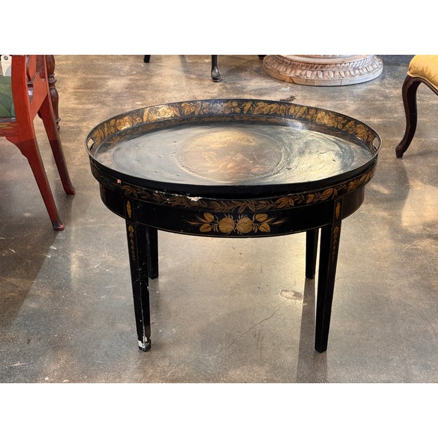 Round tole tray with a raised rim and side handles, decorated with painted floral bands along the edge and apron. The tray...