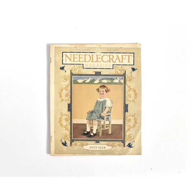 An antique or vintage July 1924 edition of "Needlecraft Magazine", featuring a little girl on the cover in a handmade...