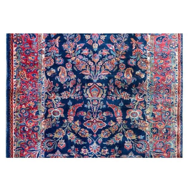 An early 20th century Persian Kashan rug with a mirrored pattern containing myriad flowers woven in reds, blues, golds,...