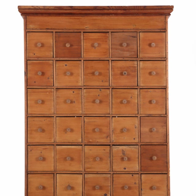 Fitted with 55 small drawers, this cabinet is constructed from pine and retaining a warm, timeworn finish. Molded details...