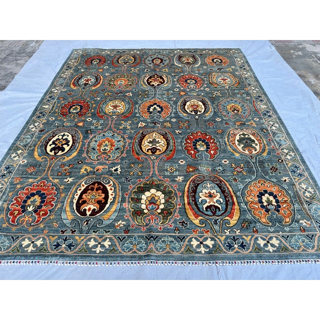 This artistic hand-knotted wool area rug features a vibrant and highly sought-after Suzani design. The main field is...