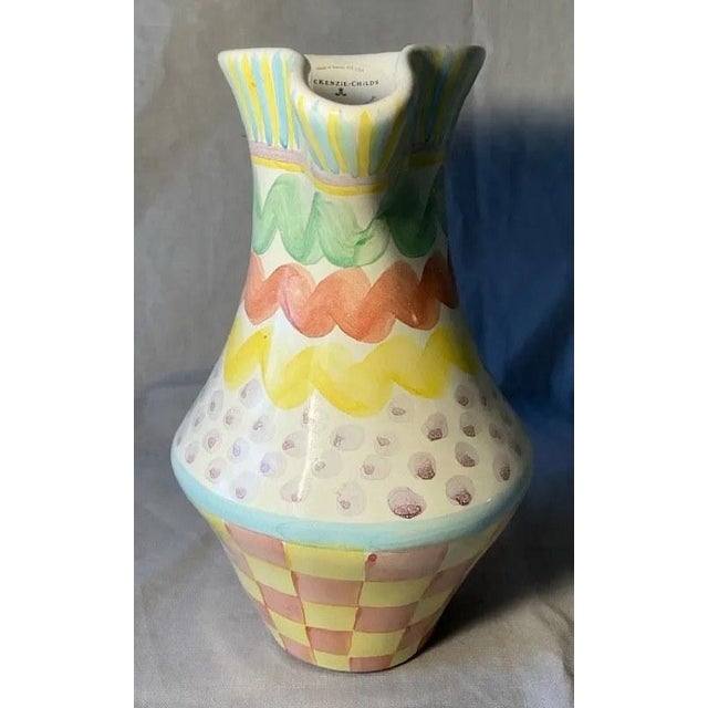 A MacKenzie-Childs Aurora pitcher, hand-painted with yellow and blue stripes at the rim, green, coral and yellow waves,...