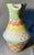 A MacKenzie-Childs Aurora pitcher, hand-painted with yellow and blue stripes at the rim, green, coral and yellow waves,...