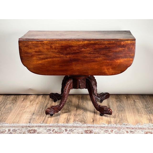 This striking antique American Empire drop leaf table dates to around 1840 and showcases the bold sculptural character...