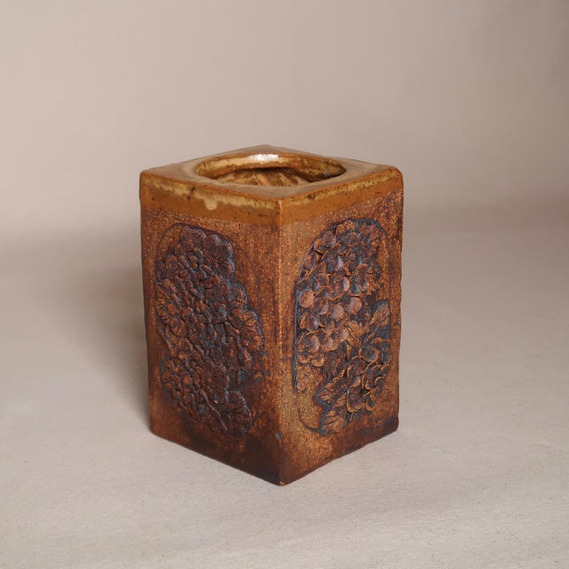 This striking handbuilt ceramic vase features a square form adorned with deeply textured floral reliefs on each side,...