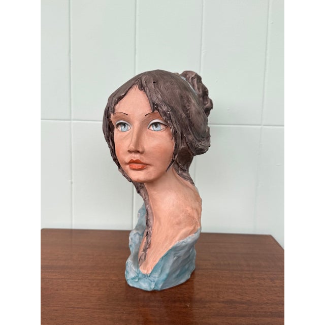 This sculpture is a female bust created in a style reminiscent of 20th-century polychrome terracotta or ceramic works. The...