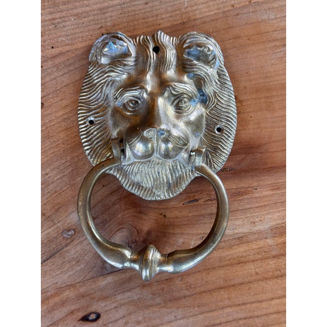 English brass door knocker cast as a lion's face with a finely combed mane, rounded ears and a textured beard. A plain...