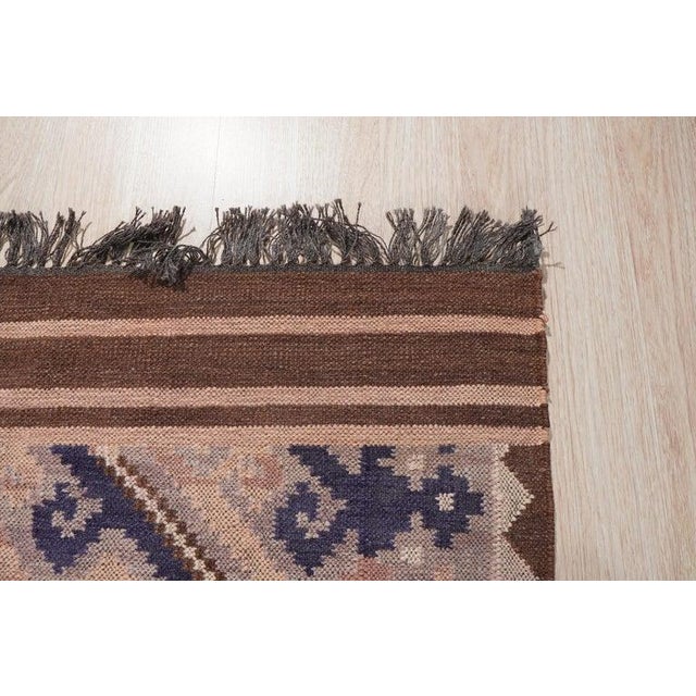 This brown earth tone wool rug features a durable flat weave construction suitable for residential spaces. Modeled after...
