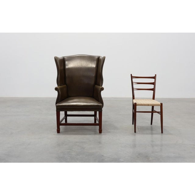A refined British mid‑century wing back armchair, upholstered in deep olive‑green leather with a beautifully aged patina....