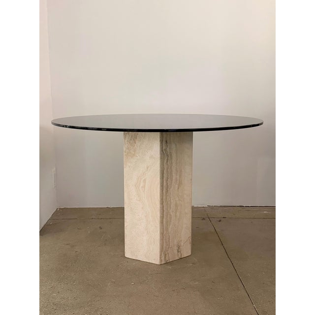 A travertine and smoked glass dining or center table. Circular smoked glass sits upon a hollow travertine pillar base.