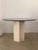 A travertine and smoked glass dining or center table. Circular smoked glass sits upon a hollow travertine pillar base.