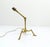 A tripod brass lamp base with an articulated structure, resting on three angled feet characteristic of the Arts & Crafts...