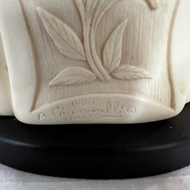 Happy Buddha figurine wears a robe decorated with sunflowers. Figure is ivory color and sits on black base. Hand and foot...