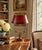 A classic bouillotte lamp rendered in warm brass, distinguished by its sculptural three horn base and tailored red tole...