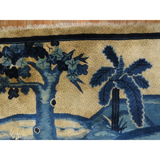 A 20th century Chinese Peking rug with 2 reindeers and a large bird in a scenic background with a tree and palm tree. The...