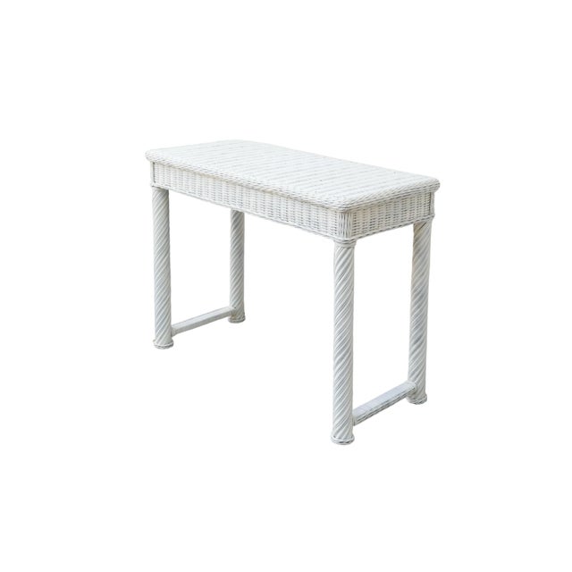 A white wicker woven hall table made of rattan. The table top is framed with a braided edge, and wooden legs and...