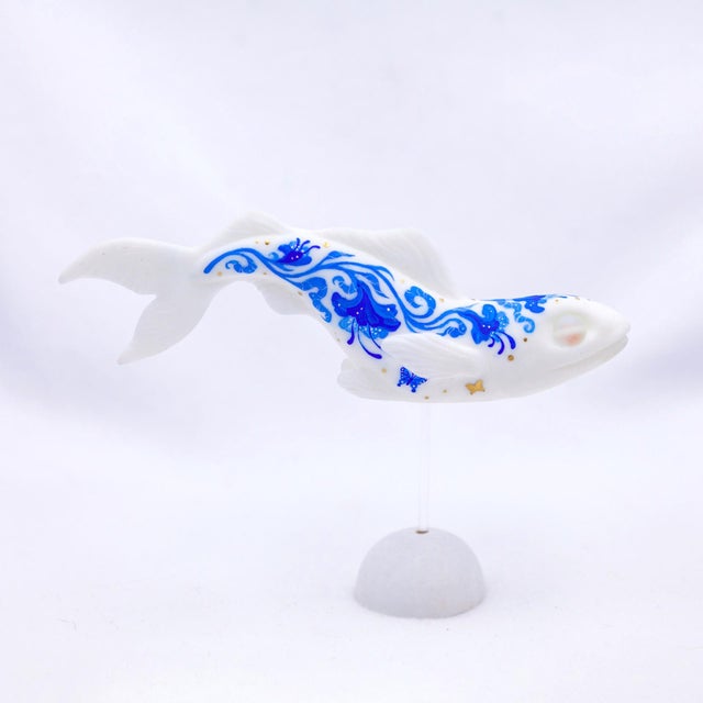 This artwork features a stylized fish rendered in a glossy white resin cast, adorned with intricate blue and gold patterns...