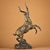 Dynamic archaic-style bronze sculpture of a leaping antelope, posed mid-stride upon a textured rock base. The body is...