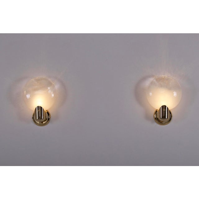 Pair of solid brass wall sconces featuring two opalescent glass globes in the shape of a rounded and flattened disc....