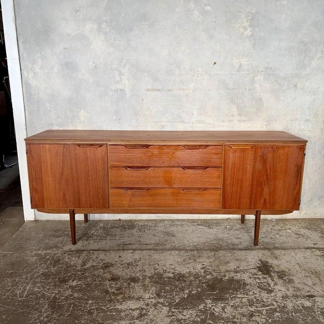 A generous 1960s teak sideboard by Austinsuite, designed by Frank Guille, with sculpted recessed handles and refined...