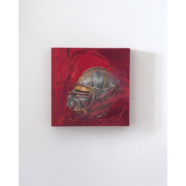 The artwork features a striking representation of a helmet-like form, rendered in rich, metallic hues against a deep red...
