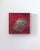 The artwork features a striking representation of a helmet-like form, rendered in rich, metallic hues against a deep red...