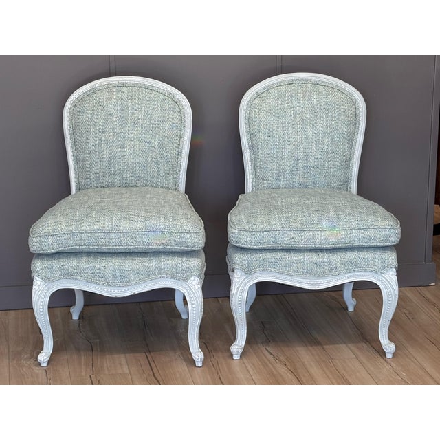 A pair of mid-20th century Louis XVI style slipper chairs with painted frames and carved detailing along the seat rails...