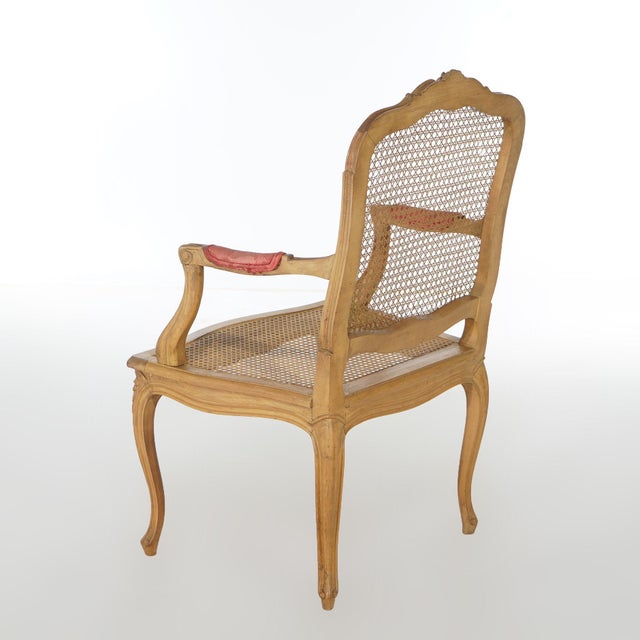 An antique French Louis XV style arm chair offers carved fruitwood frame having floral crest over caned seat and back,...