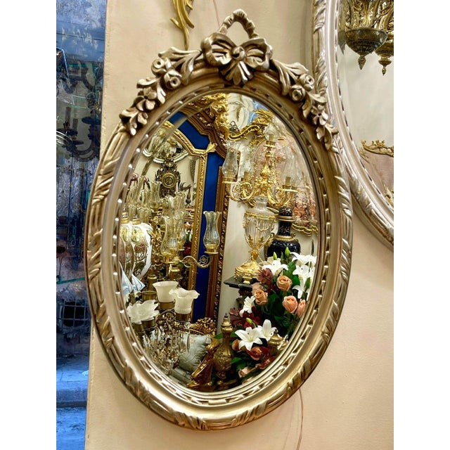Elegant French-style oval wall mirror featuring a richly hand-carved frame with intricate ornamental detailing and a...
