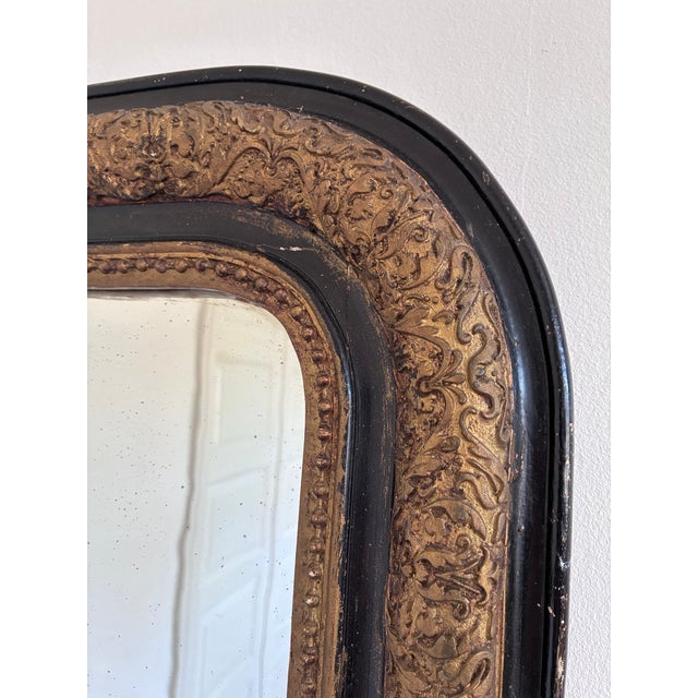 This antique French Louis Philippe mirror dates from the 19th century and showcases a black and gold frame with raised...
