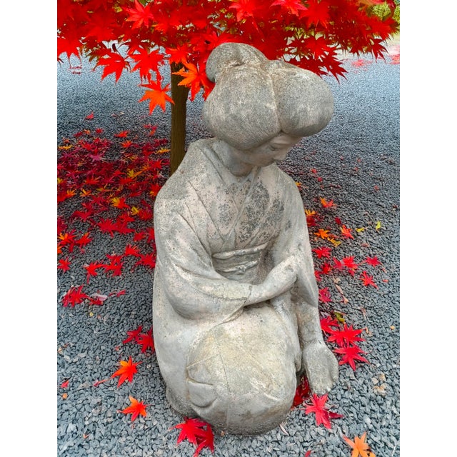 Graceful vintage cast concrete Geisha statue depicting a woman in a traditional kimono, seated in quiet contemplation. The...