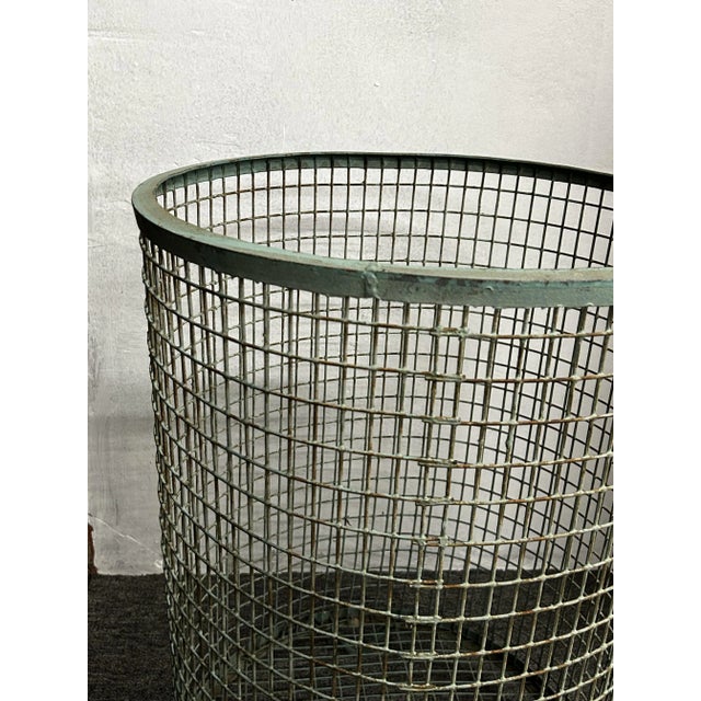 This cylindrical basket is made from galvanised wire mesh, featuring a round base and flared top edge. It has a green...
