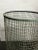 This cylindrical basket is made from galvanised wire mesh, featuring a round base and flared top edge. It has a green...