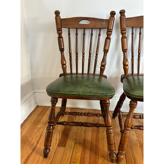 Pair of mid-20th century Virginia House Windsor-style oak chairs. Feature turned wood and cleanable green faux leather...