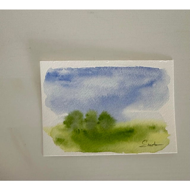 A luminous watercolor capturing a cluster of trees beneath a wide, expansive sky. Gentle washes of blue and layered greens...