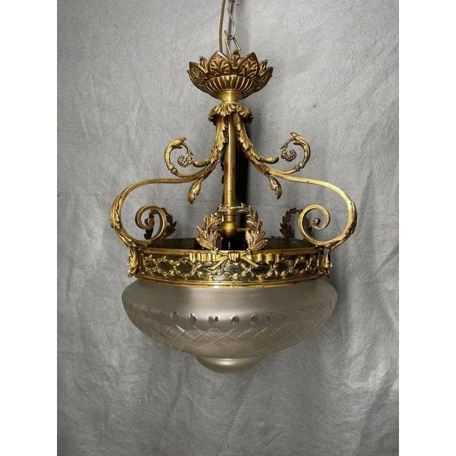 Elegant French gilt bronze pendant light with scrolling vine and leaf motifs, surmounted by a decorative crown. The...